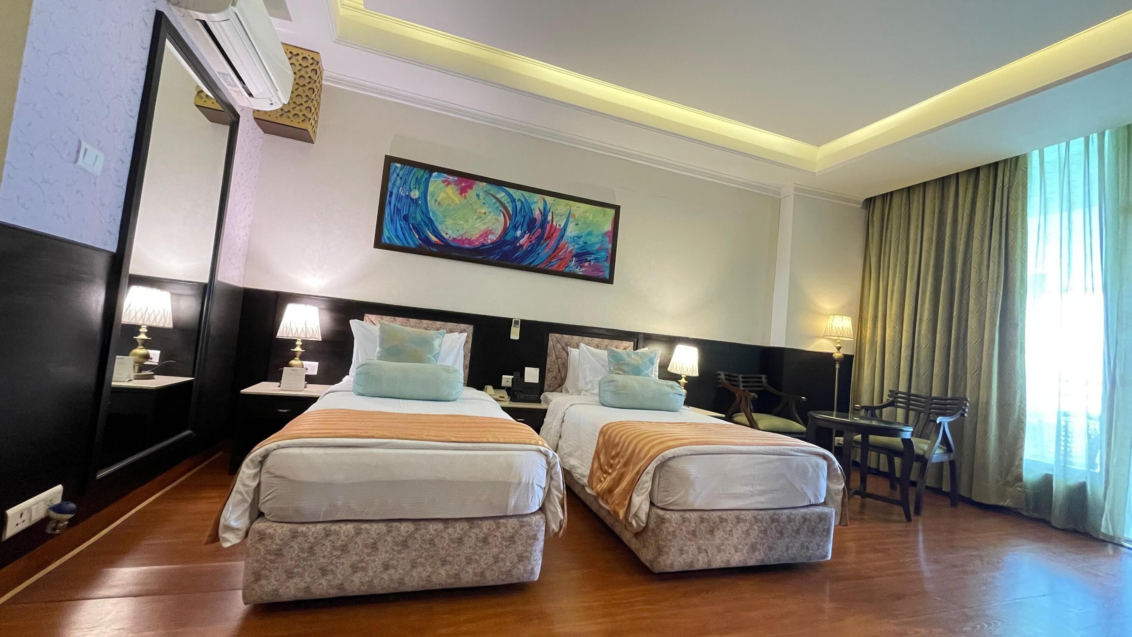 A hotel room with two beds, a painting, a desk, and a chair.
