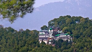 A multi-story building with a green roof, surrounded by dense forest and mountains. - Fortune Park Moksha, Mcleodganj  - Member ITC Hotels' Group (Dharamshala)