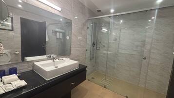 Un baño moderno con un espejo grande, un lavamanos blanco, una ducha con mampara de vidrio y un mueble de tocador negro.