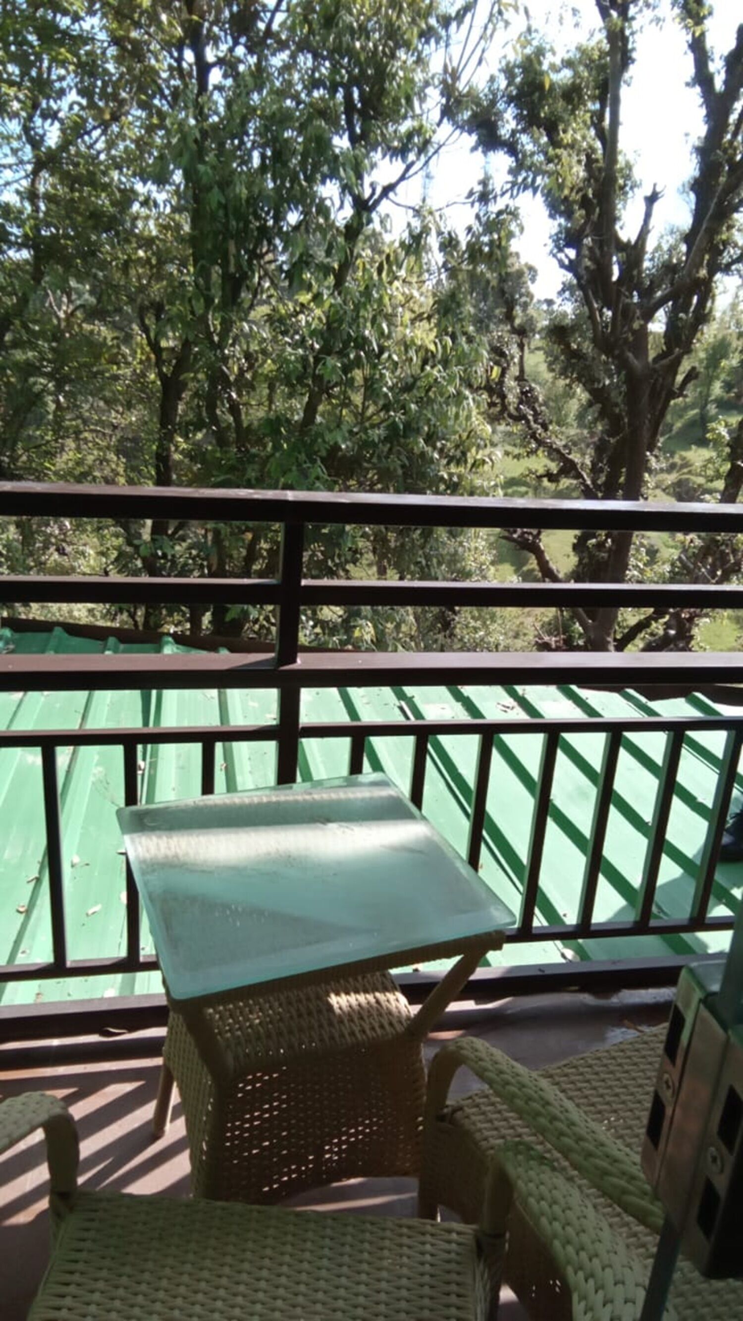 Un balcon avec une table et des chaises, donnant sur un espace vert arboré.