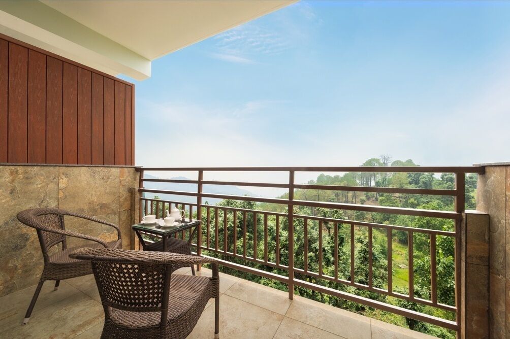Un balcón con muebles de mimbre y una mesa, con vistas a un paisaje exuberante.
