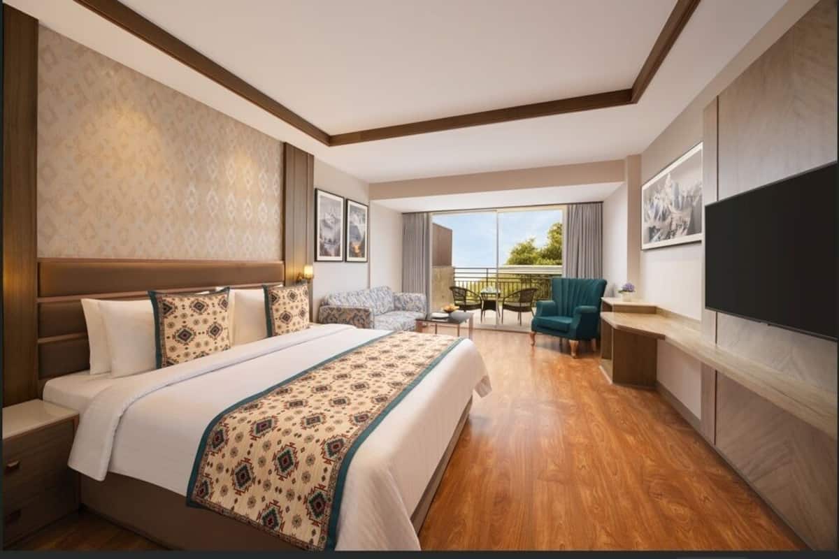 Quarto de hotel com uma cama grande, varanda com vista, televisão e área de estar.