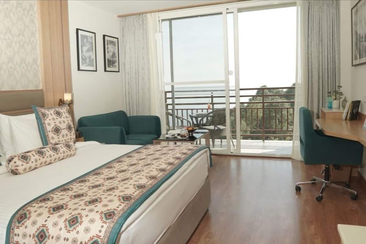 Een hotelkamer met een bed, een bureau, een stoel en een balkon met uitzicht.