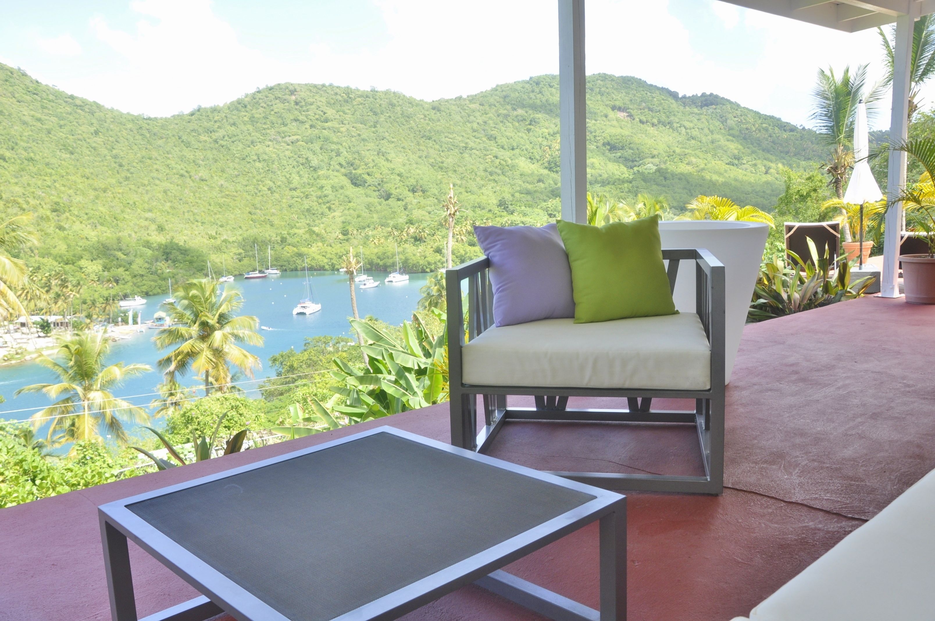 Un balcón con vista a una bahía, una silla con cojines y una pequeña mesa.