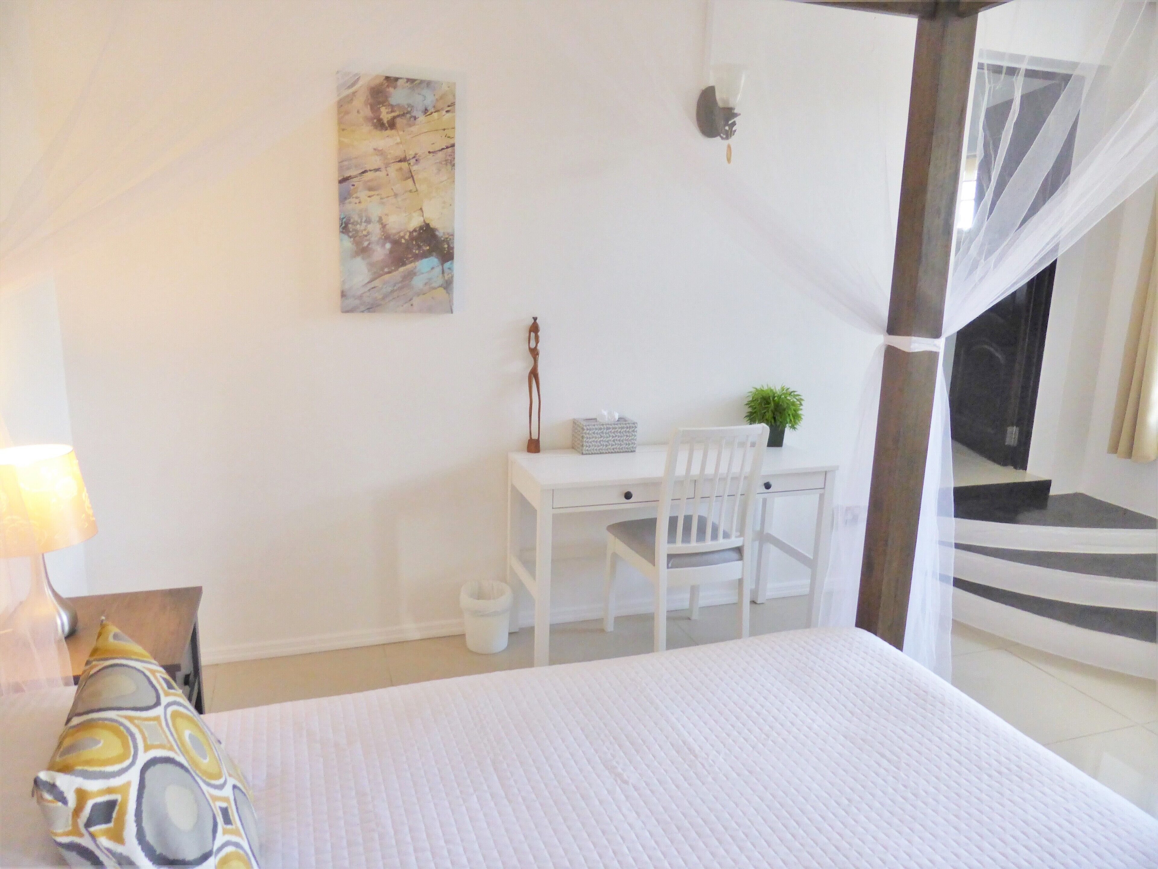 A bedroom with a bed, a desk with a chair, a small plant, and a staircase leading to an upper level.