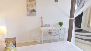 A bedroom with a bed, a desk with a chair, a small plant, and a staircase leading to an upper level.