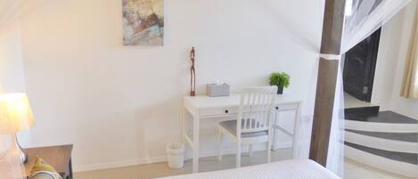 A bedroom with a bed, a desk with a chair, a small plant, and a staircase leading to an upper level.