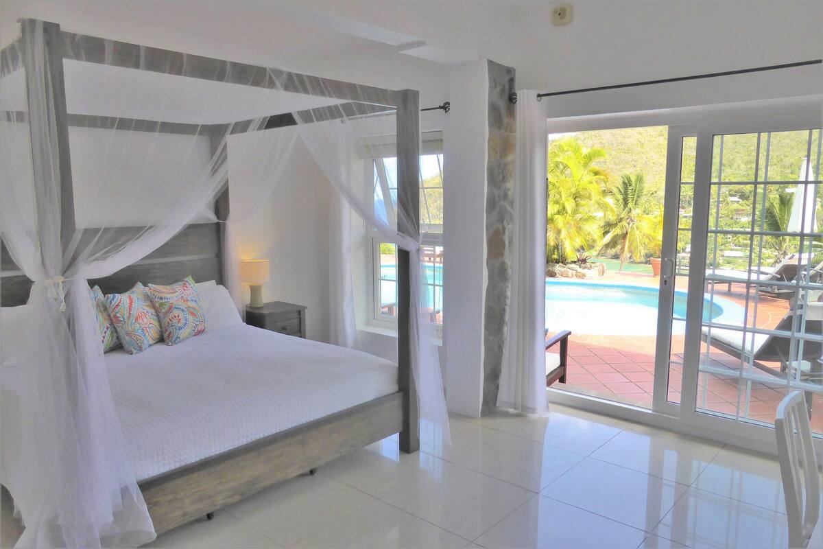 Un dormitorio amplio con una cama grande, dosel y vista a una piscina.