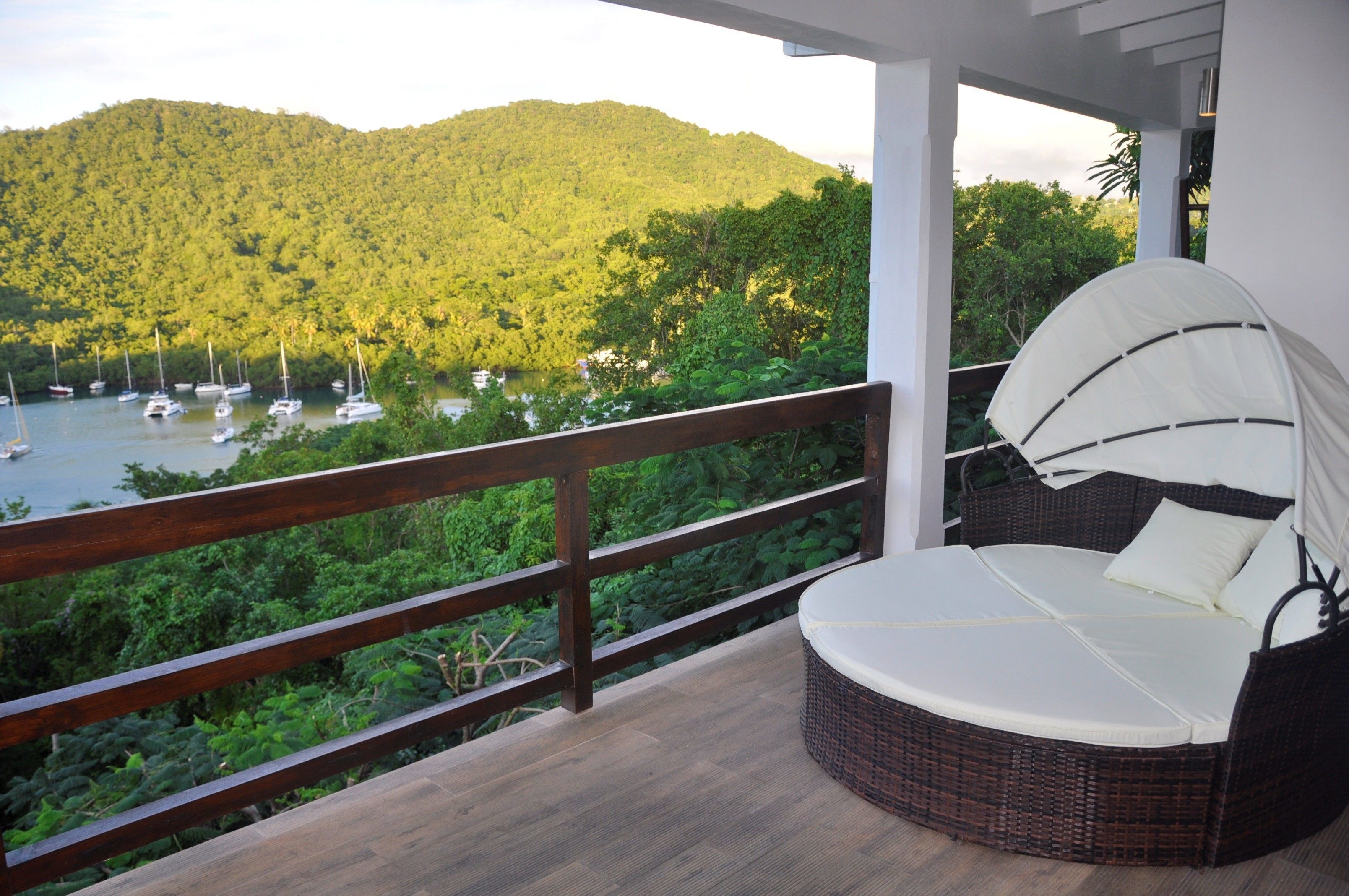 Un balcone con un divano in vimini e vista su un lago con barche.