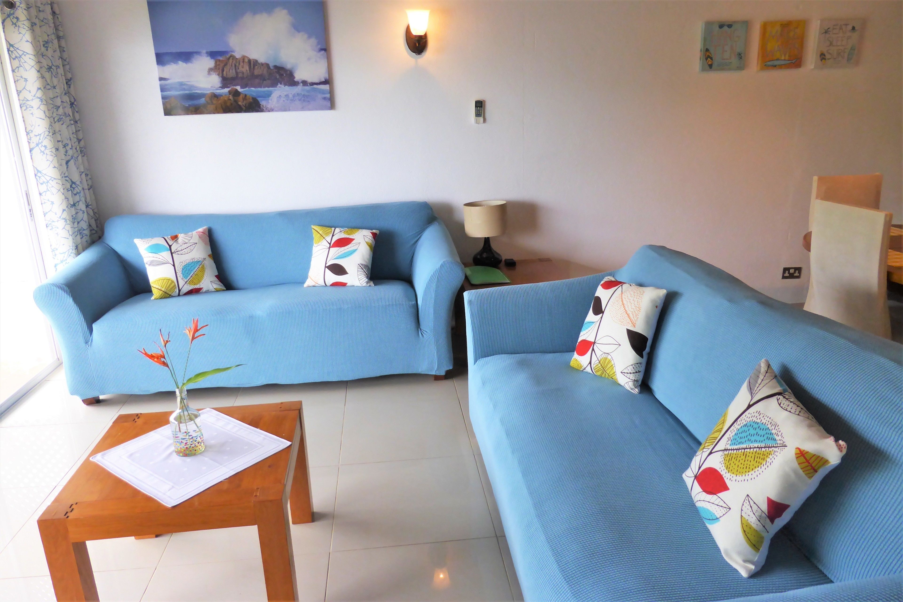A living room with two blue sofas, a wooden coffee table with a vase, and a lamp on a side table.