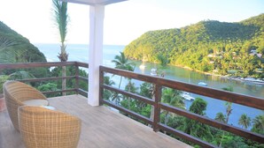 Terraza de madera con mobiliario de mimbre, con vista a un río y una colina con casas.