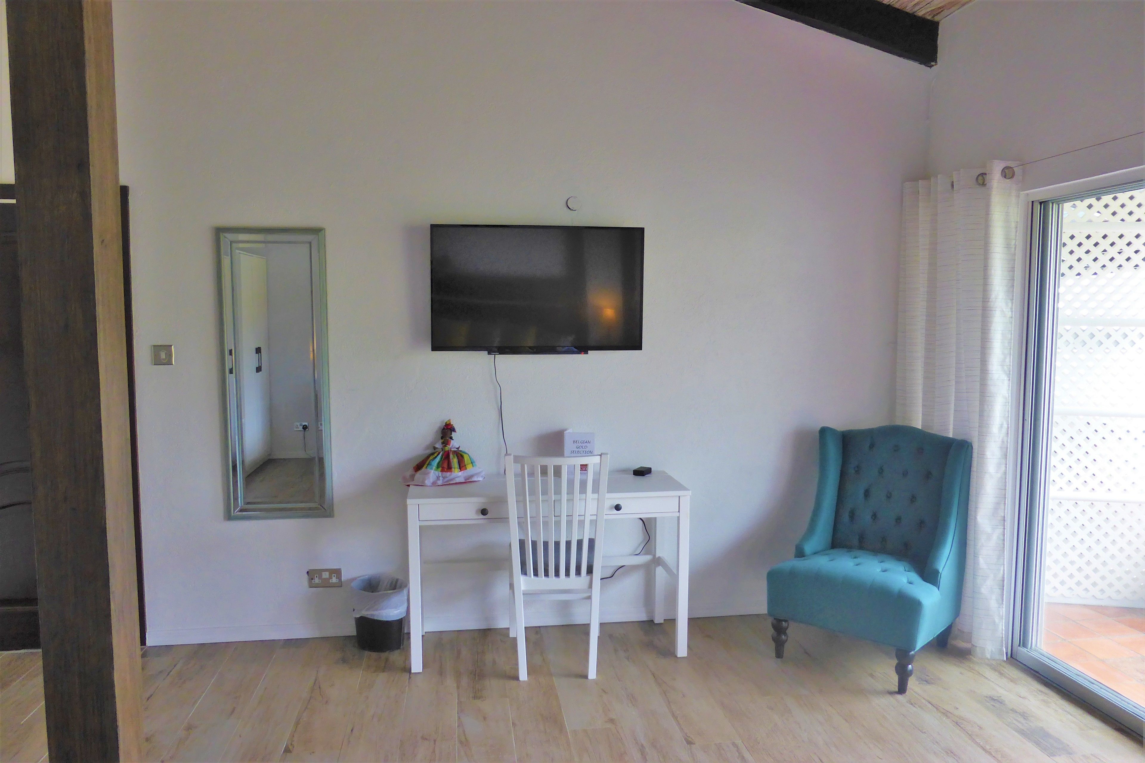 Een kamer met een wit bureau, een blauwgroene fauteuil, een aan de muur bevestigde televisie en een raam met uitzicht.