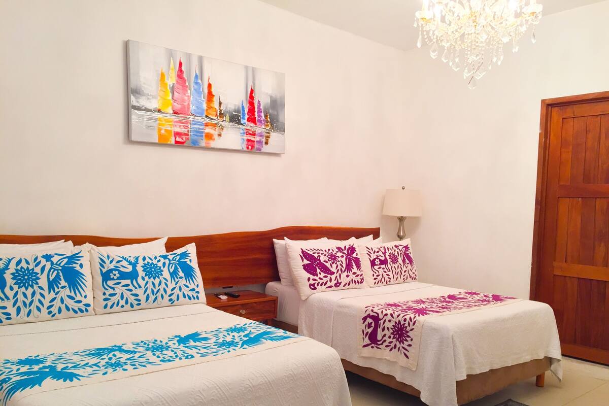 A hotel room with two beds, a wooden headboard, a chandelier, a painting on the wall, and a wooden door.