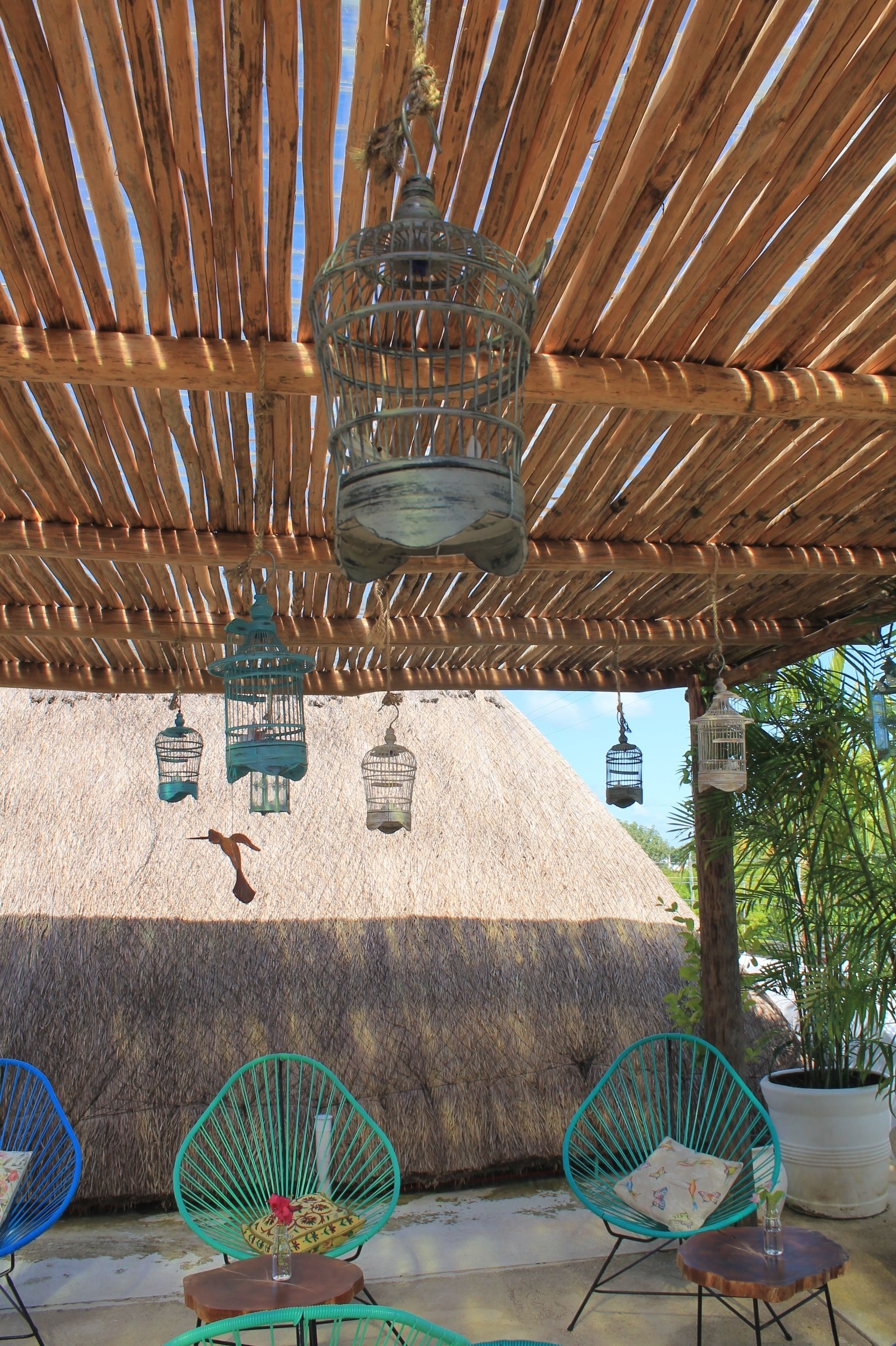 A thatched-roof outdoor area with wicker chairs and hanging birdcages.