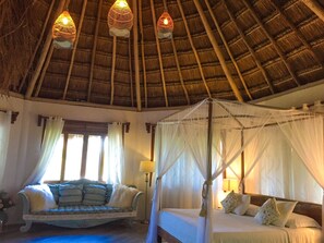 A room with a thatched roof, a bed with a canopy, a sofa with cushions, and a window with curtains. - Toto Blue Hotel Boutique (Bacalar)