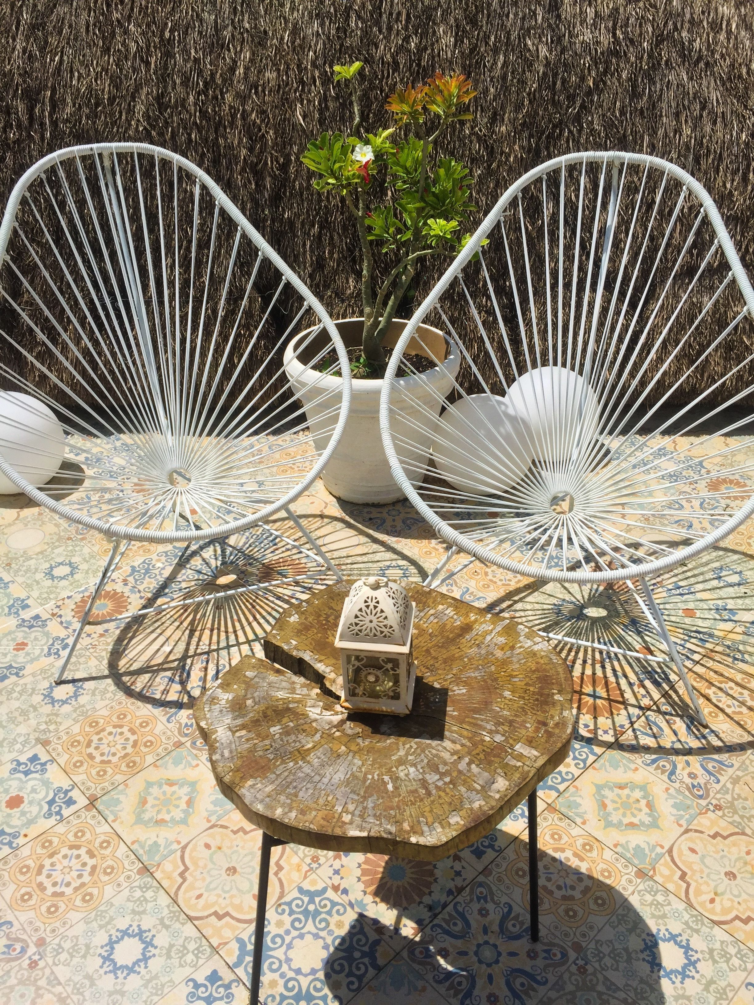 Two white wire-framed chairs, a small table with a lantern, and a potted plant with a white flower.