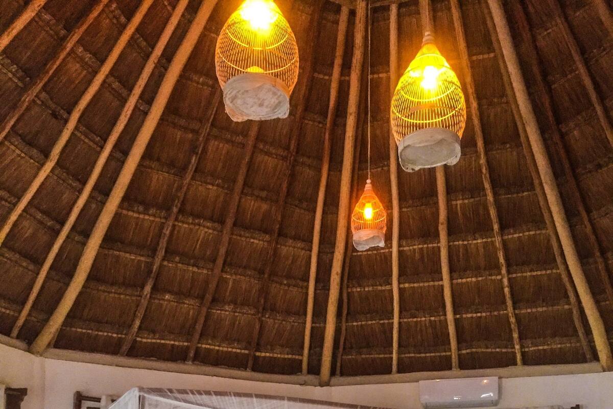 A room with a bed, a blue sofa, and a thatched roof.