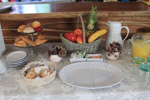 Une table de petit-déjeuner avec des viennoiseries, des fruits, une carafe et un verre de jus d’orange.