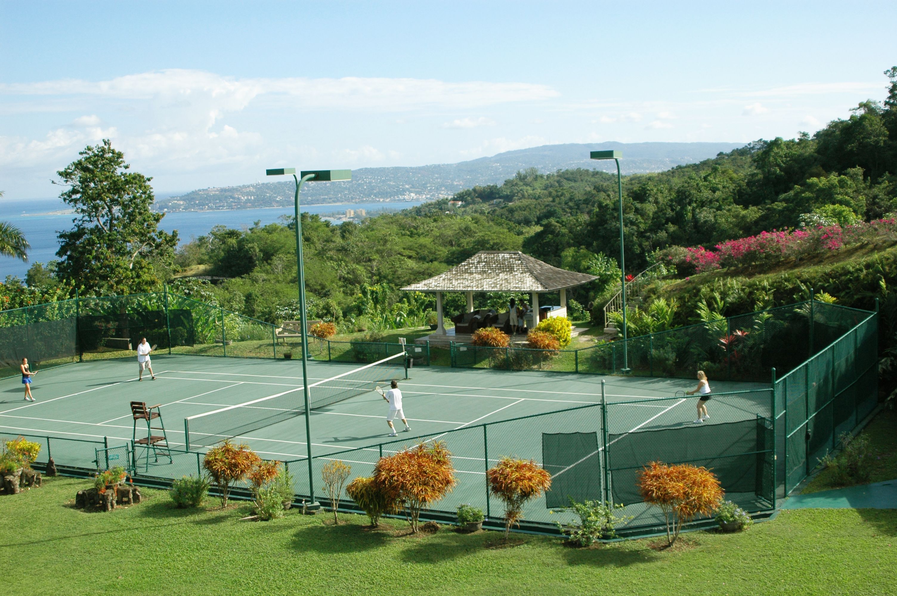 Una cancha de tenis con vista al mar y colinas al fondo.