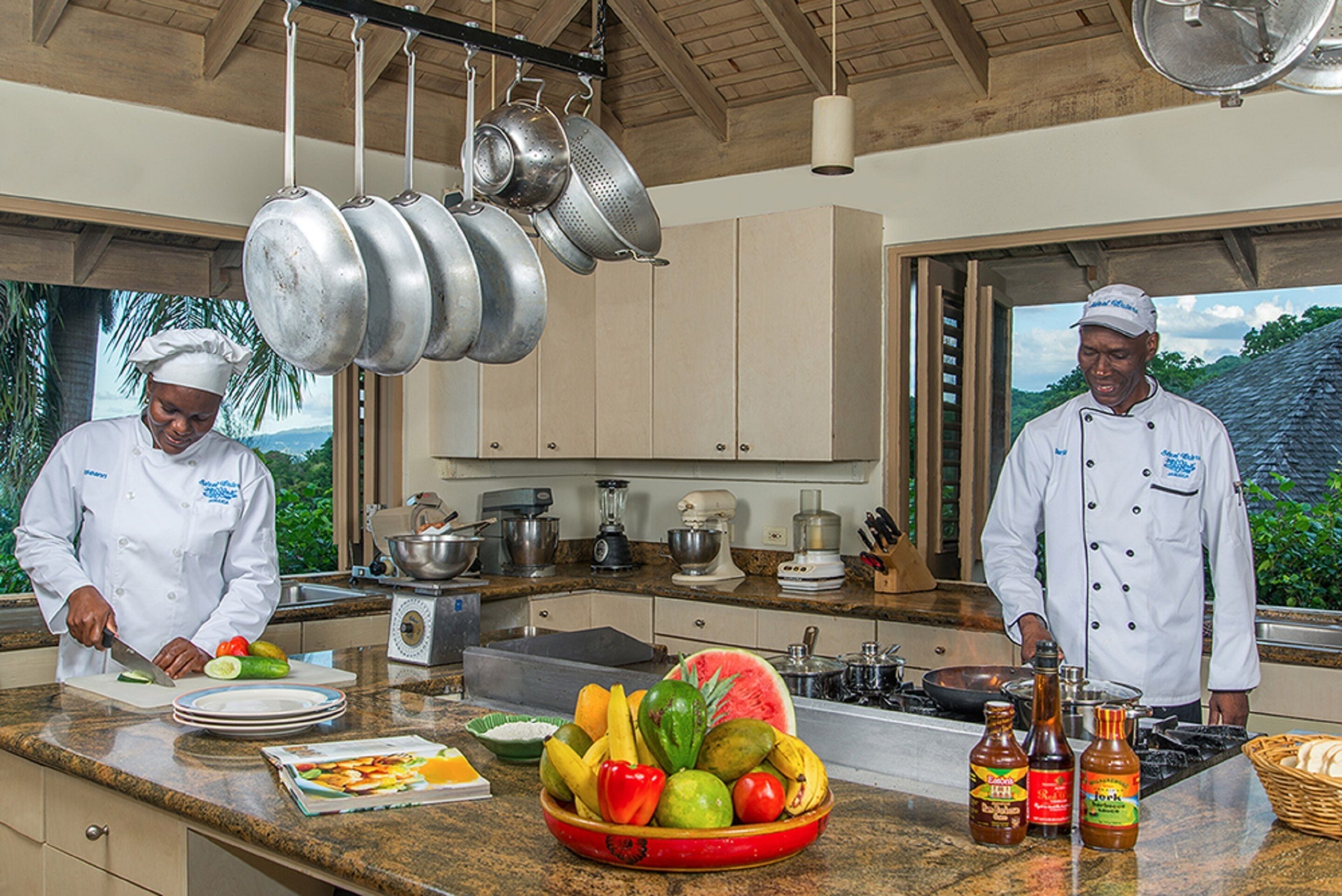 Una cocina con dos chefs preparando comida, un frutero y varios electrodomésticos.