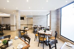 Un comedor moderno con varias mesas y sillas, un ventanal grande y un televisor de pantalla plana montado en la pared.