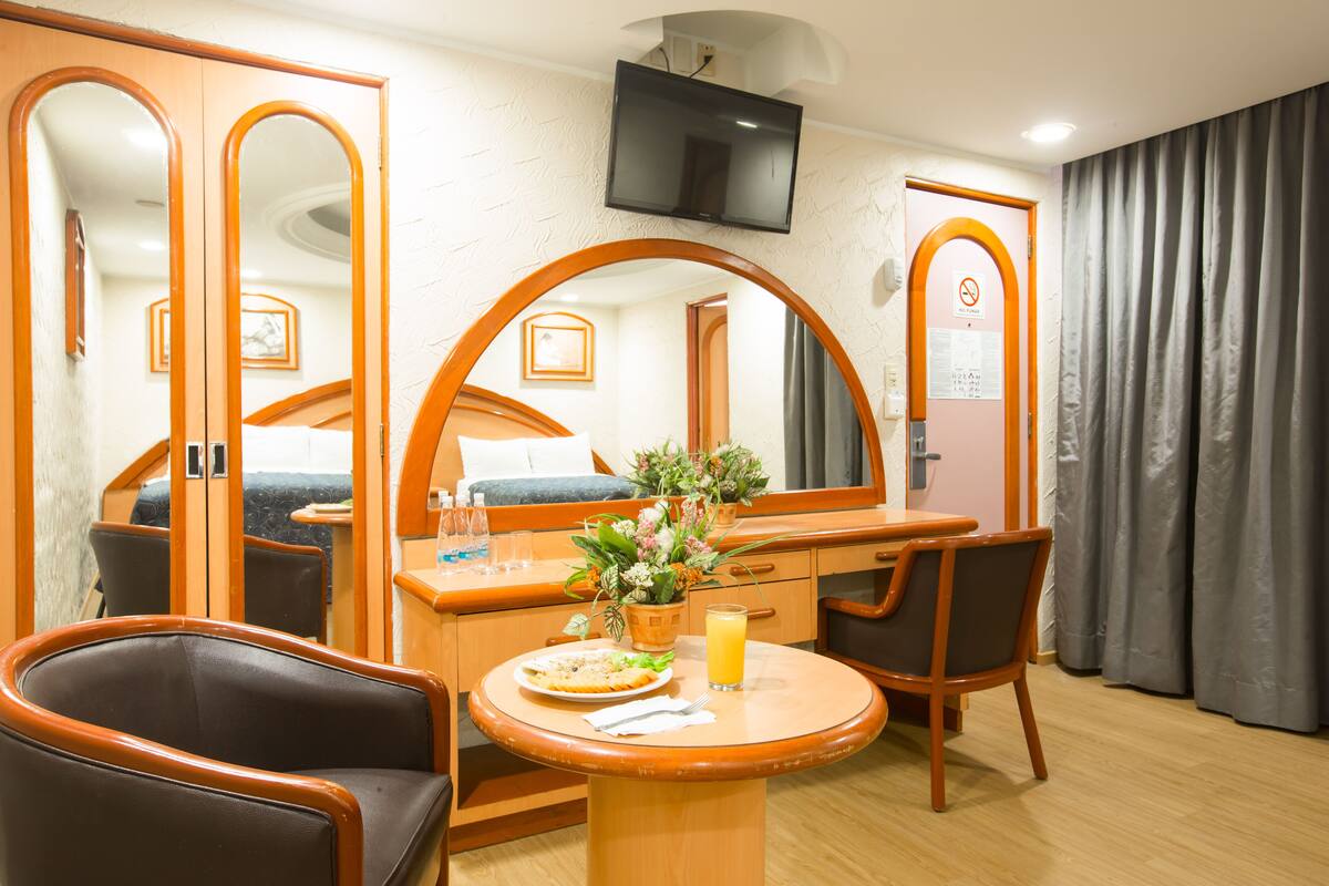 A hotel room with a bed, a desk, a chair, a TV, and a window with curtains.