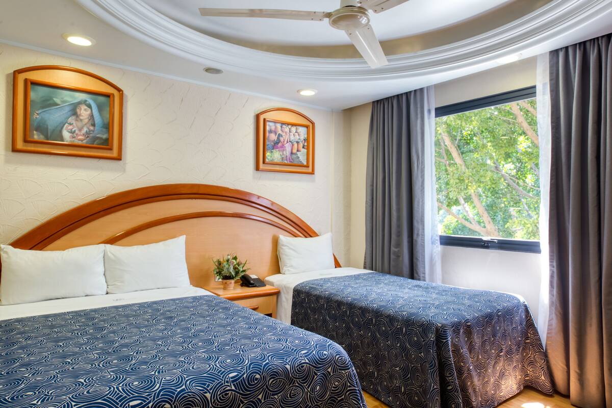 A hotel room with two beds, a wooden headboard, a ceiling fan, and a window with curtains.