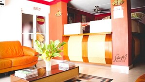 A hotel reception area with a reception desk, a sofa, a coffee table with magazines, and a plant. - Seven Stars Hotel (Port-au-Prince)
