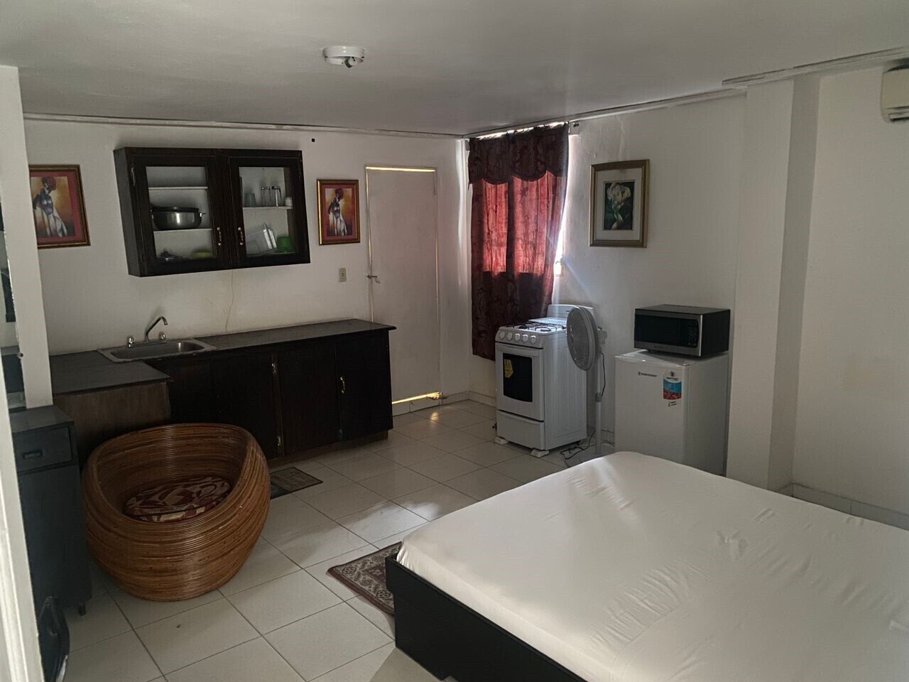 A hotel room with a bed, a small kitchenette, a sink, a stove, a microwave, and a large woven basket.