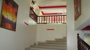 A staircase with a wooden railing, a ceiling fan, and red accents on the walls. - Seven Stars Hotel (Port-au-Prince)