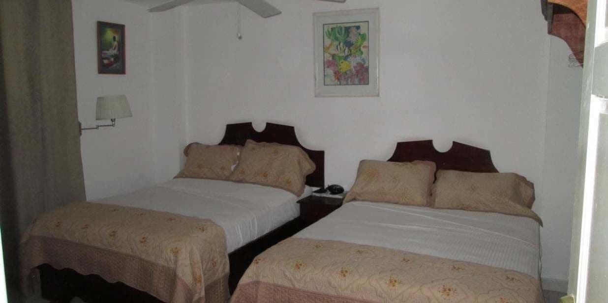 Una habitación con dos camas, cada una con cabecero de madera, una mesita de noche, una lámpara y un cuadro en la pared.