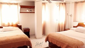 A hotel room with two beds, a ceiling fan, and curtains on the windows. - Seven Stars Hotel (Port-au-Prince)