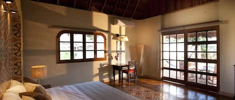 A bedroom with a bed, a desk, and a chair. There are windows and a ceiling fan.