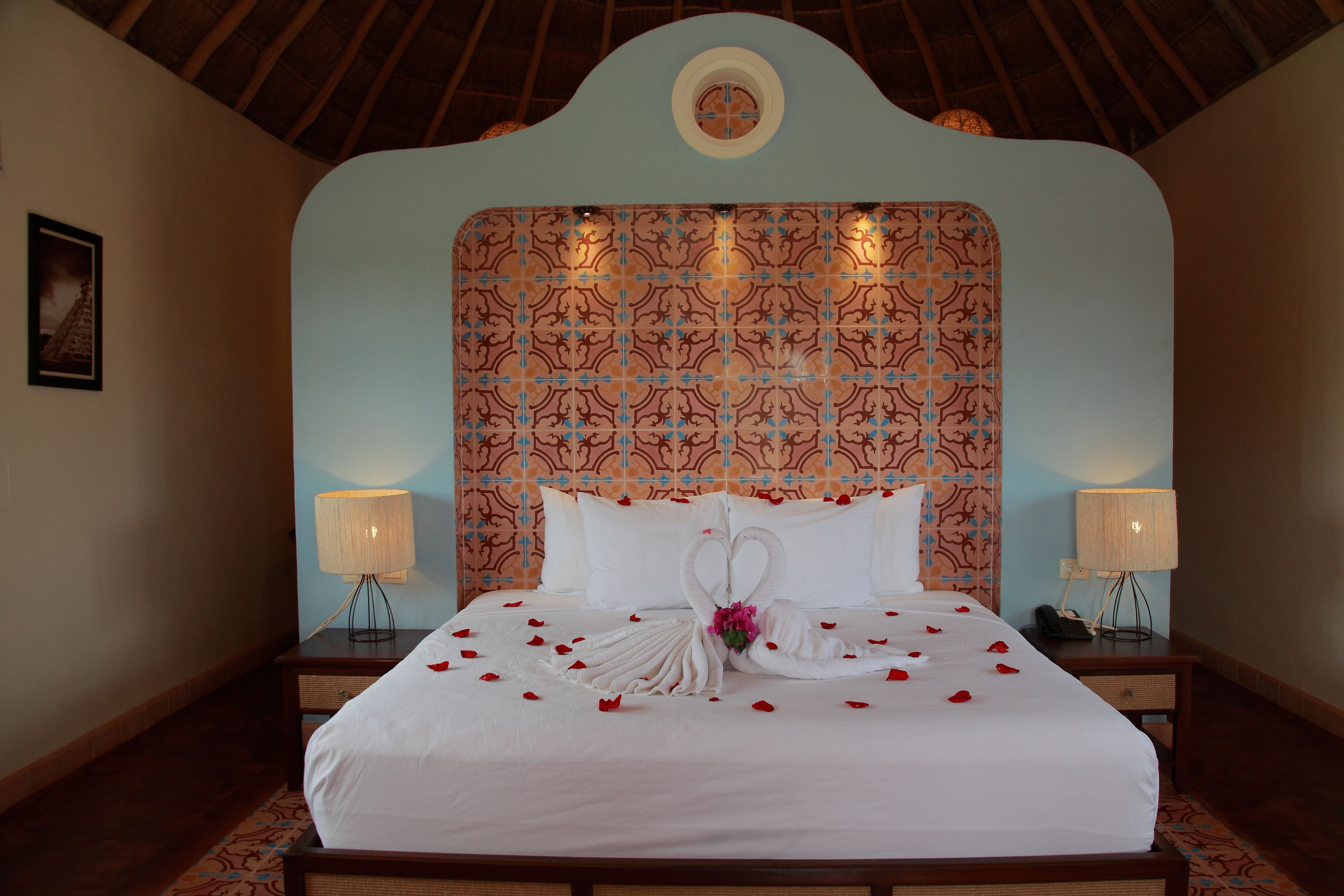 A hotel room with a large bed, two bedside tables, a patterned headboard, and a framed picture on the wall.