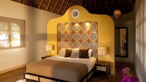Ein Schlafzimmer mit Bett, Nachttischlampen, einem Nachttisch, einem gemusterten Boden, einem Deckenventilator und einem Fenster mit Tageslicht.
