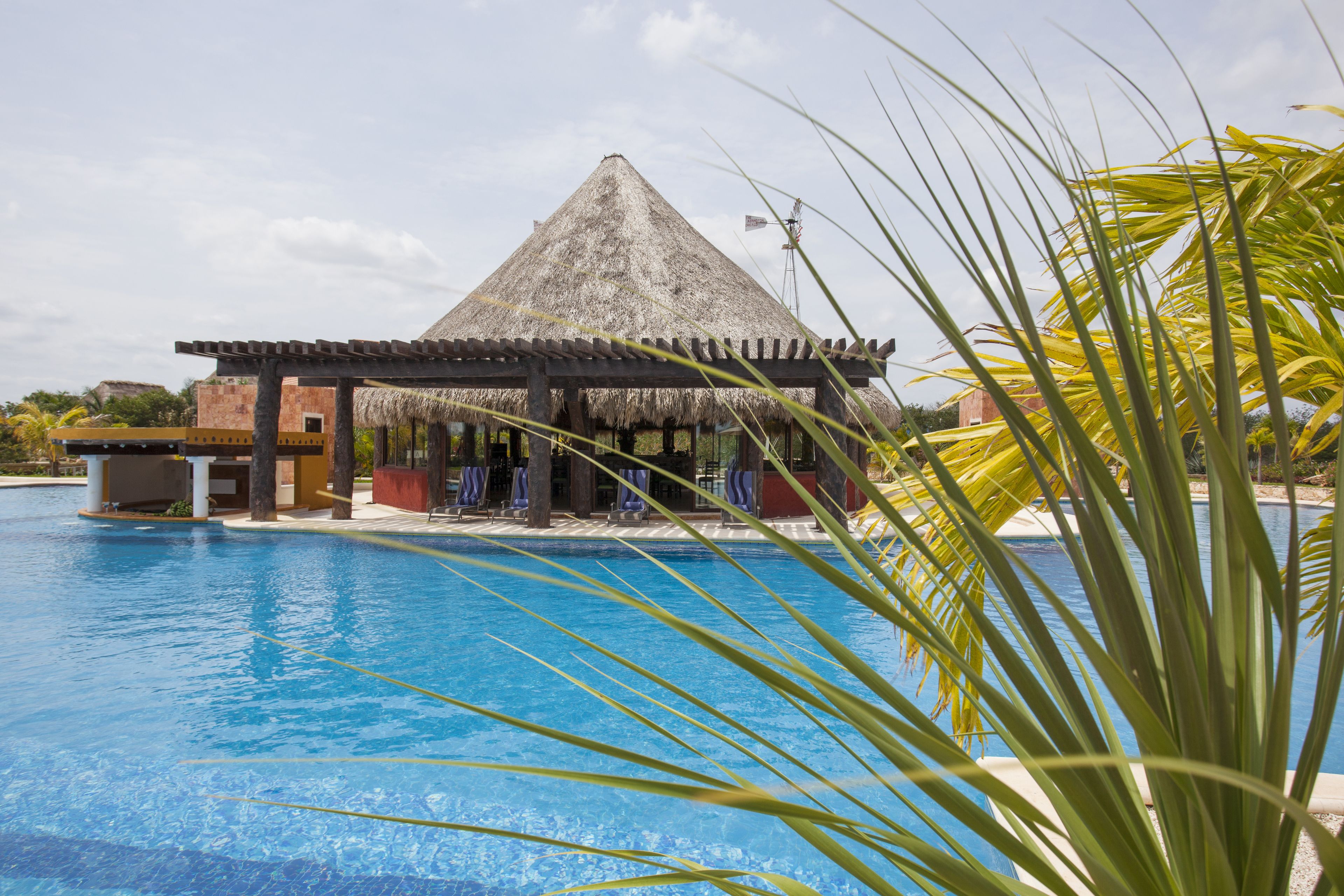 A pool area with a thatched-roof structure, lounge chairs, and a clear blue pool.