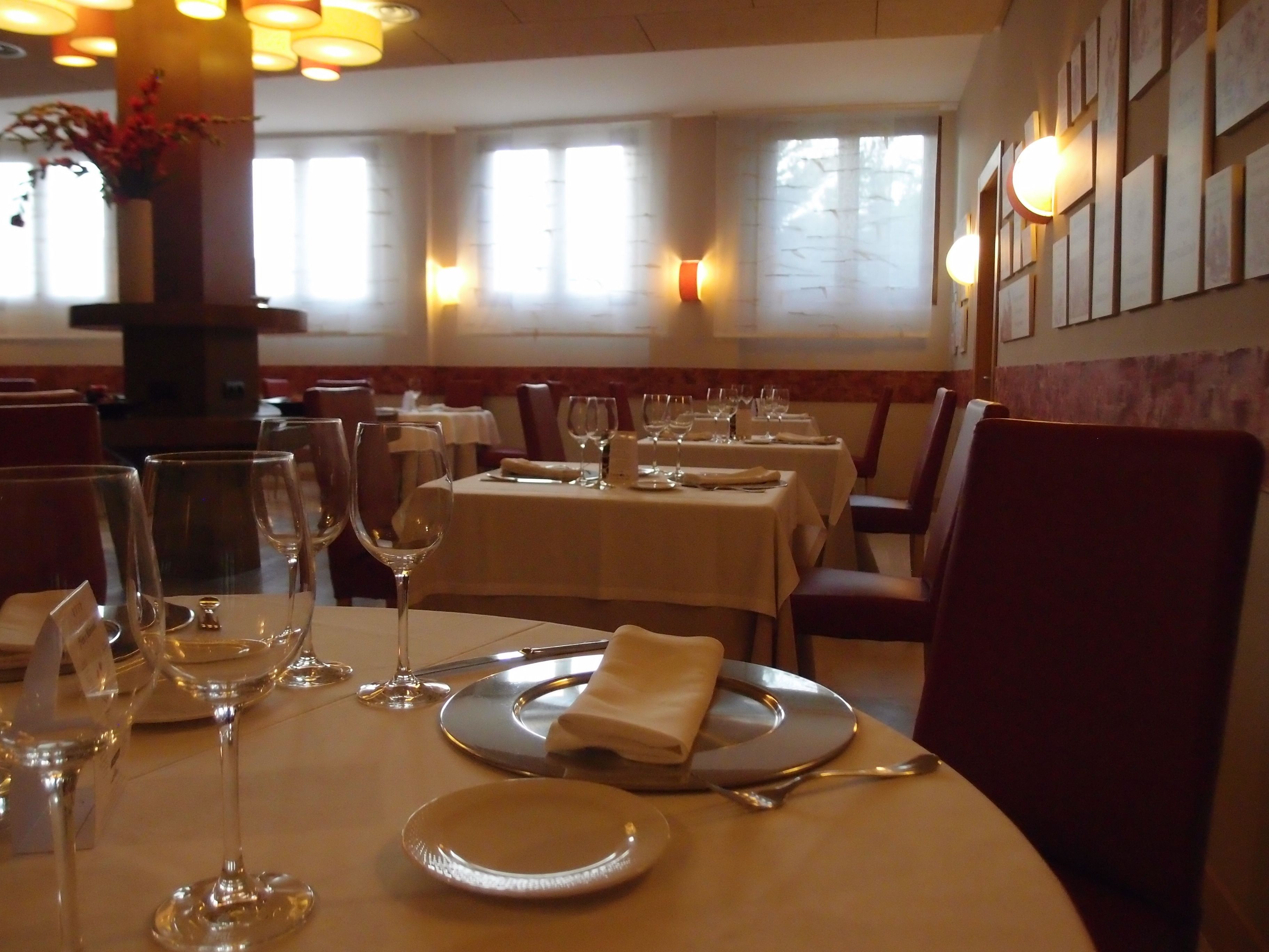 Interior de restaurante com mesas montadas para refeição, incluindo pratos, copos e talheres.
