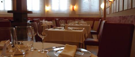 Interior de restaurante con mesas preparadas para comer, incluyendo platos, vasos y cubiertos.