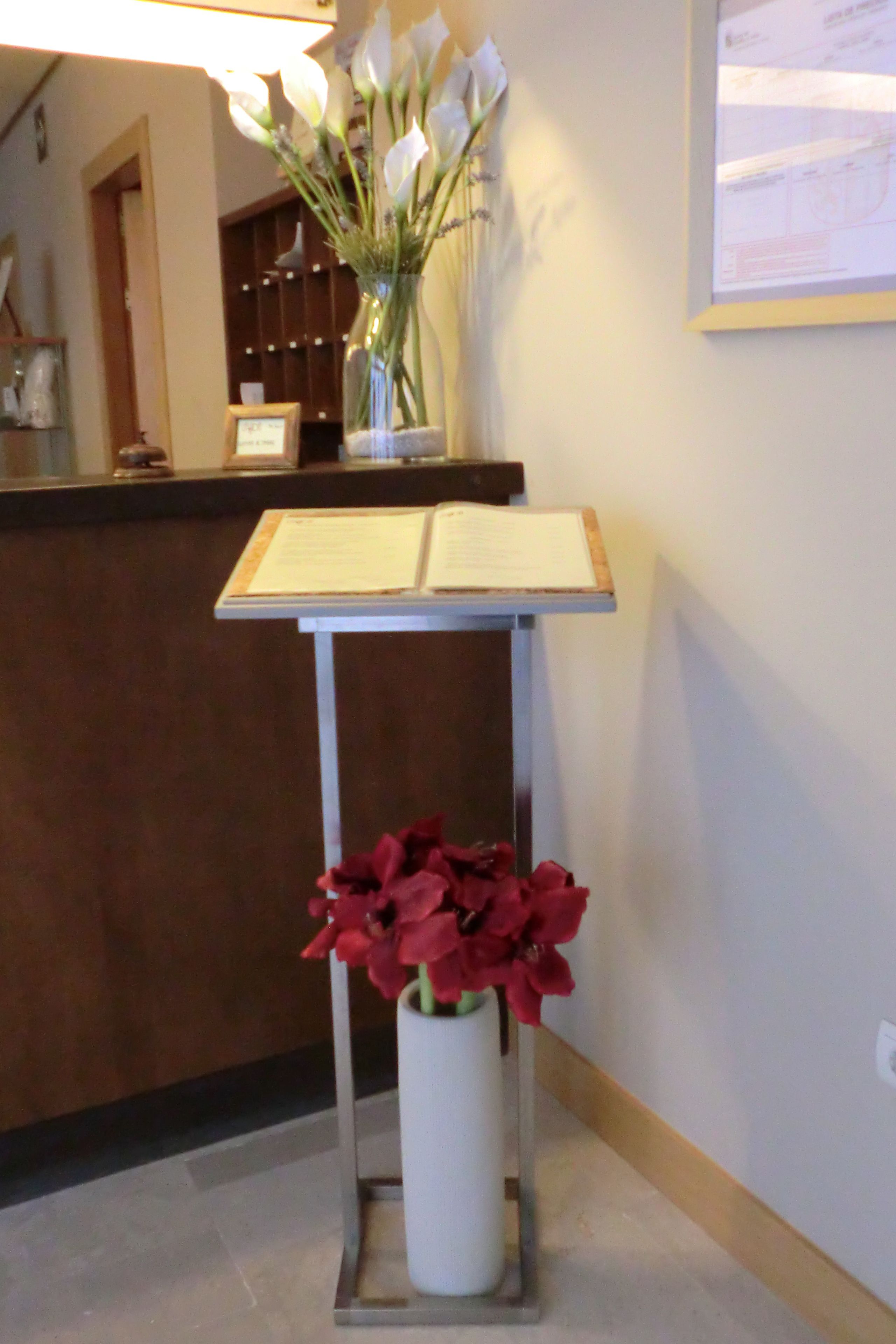 A reception desk with a vase of white flowers and a vase of red flowers.