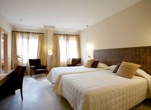 Habitación de hotel con dos camas, un escritorio, una silla y una lámpara.