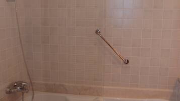 A bathroom with a bathtub, a showerhead, and a grab bar.