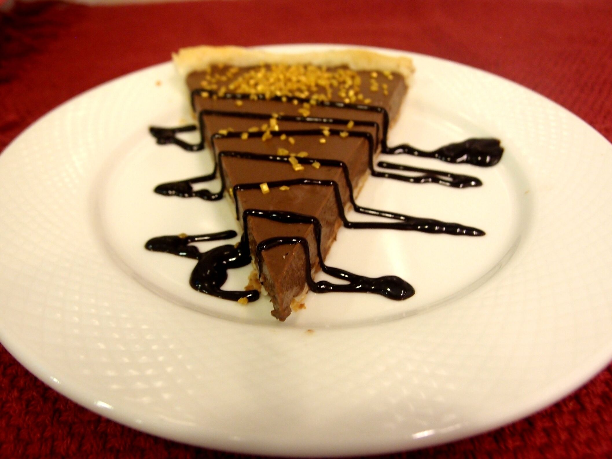 A dessert on a white plate with chocolate and caramel layers, drizzled with chocolate sauce.