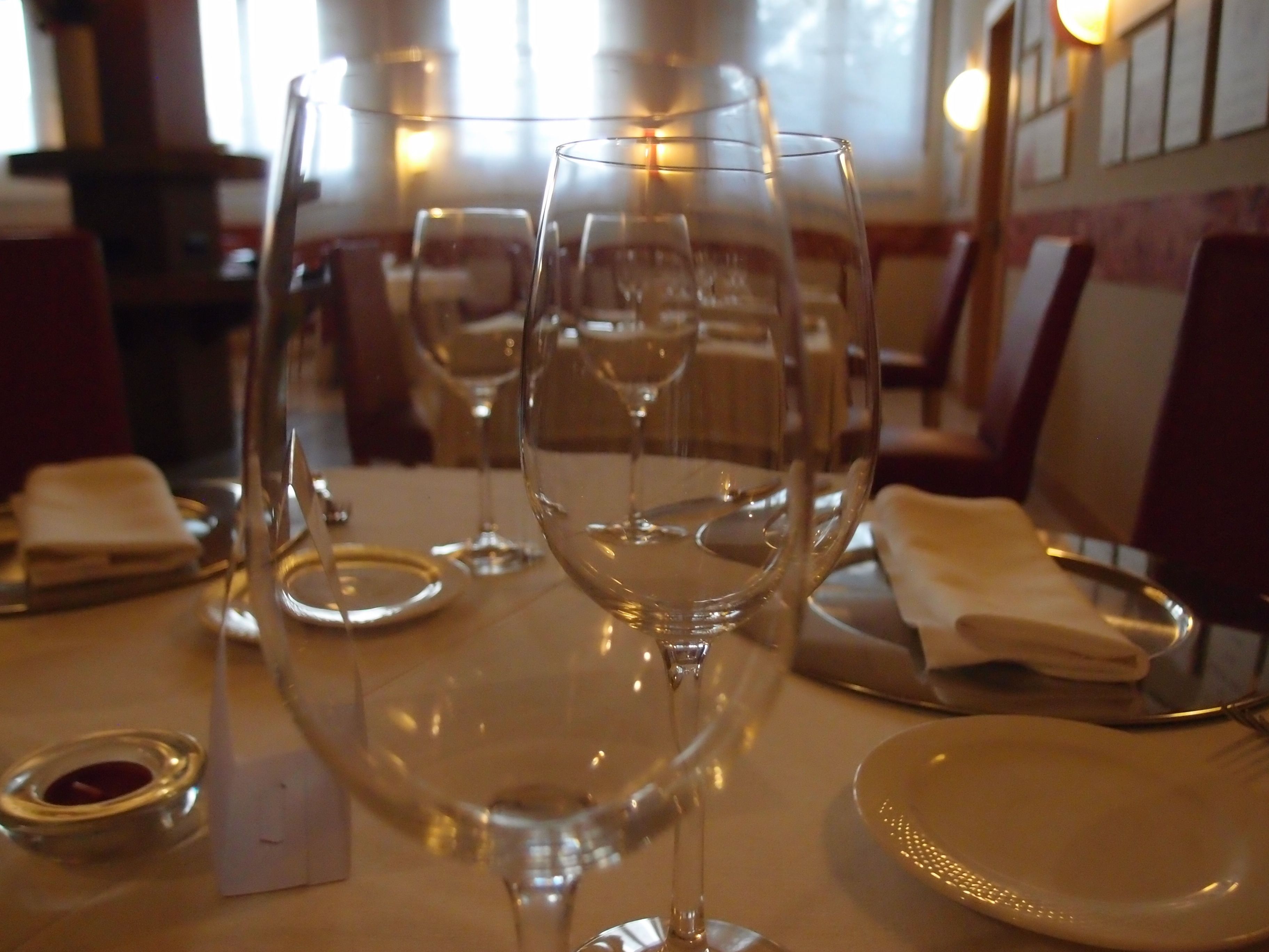 Una mesa de comedor lista con copas de vino, platos y cubiertos en un restaurante.