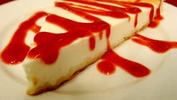 Una porción de pastel de queso con salsa roja sobre un plato blanco.