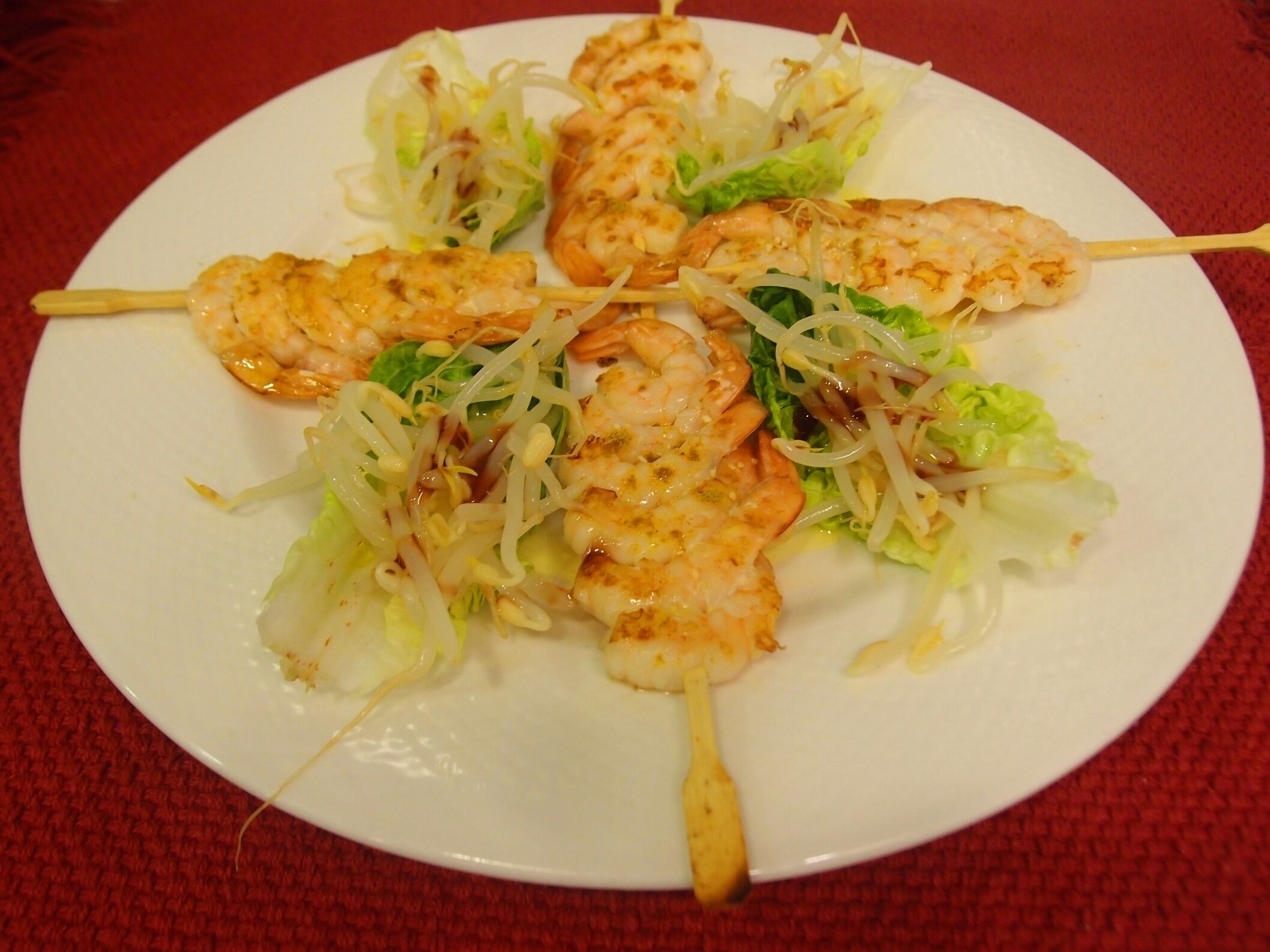 A plate of skewered chicken and shrimp with lettuce and bean sprouts.