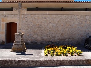 Una cruz de piedra, una puerta y un jardín con flores amarillas.