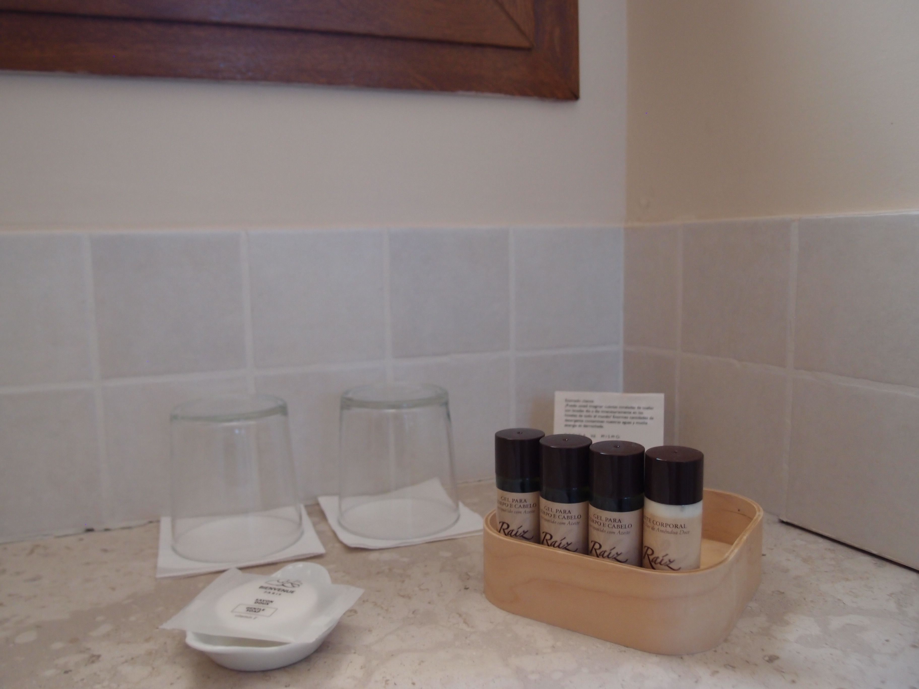Una encimera de baño con cuatro botellas de productos para el cabello, dos vasos vacíos y un pequeño recipiente blanco.