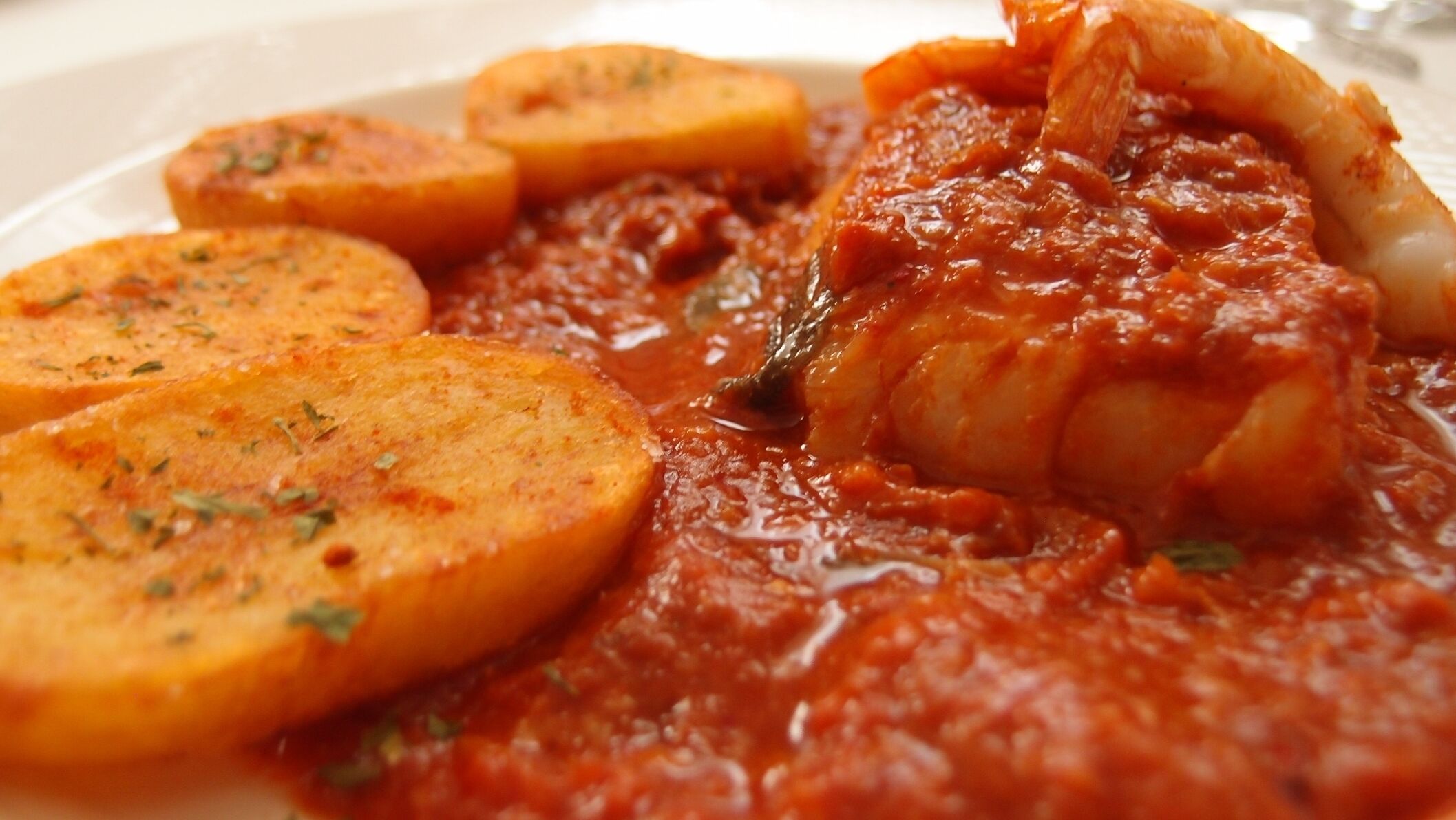 A plate with fish, potatoes, and a tomato-based sauce.