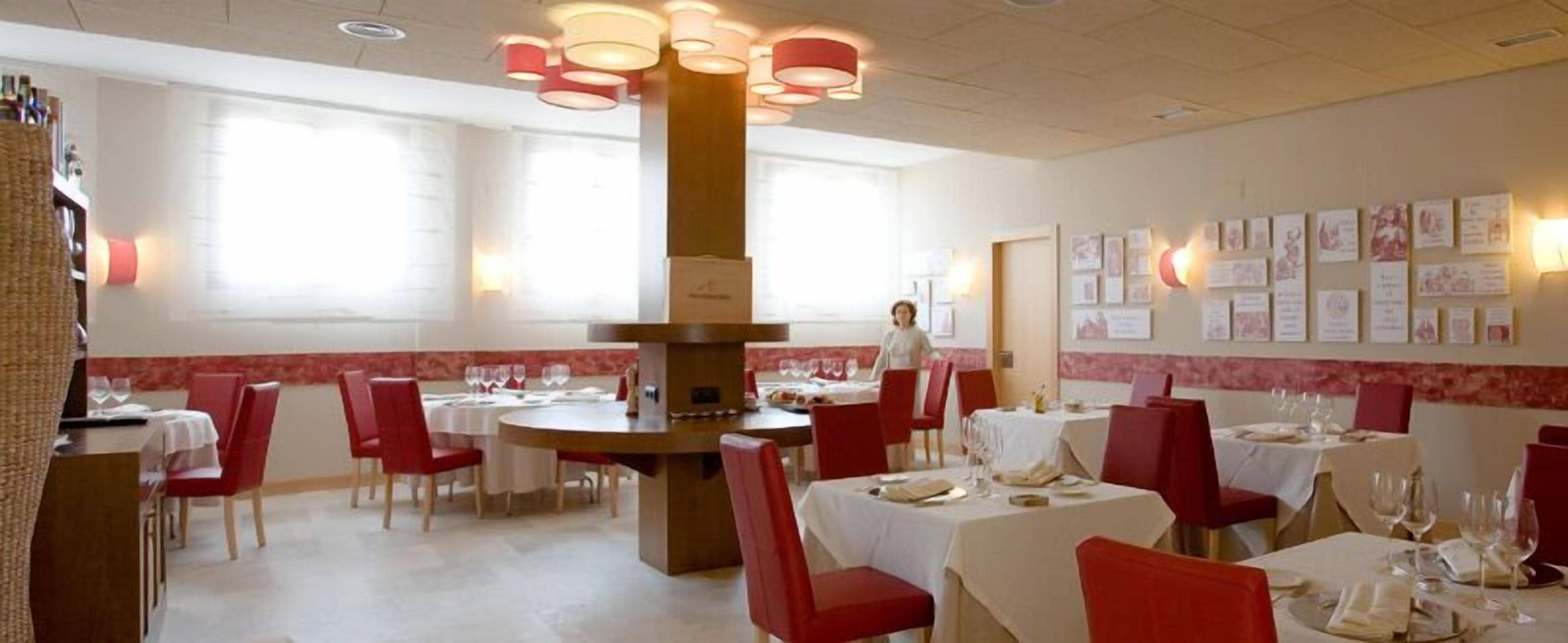 Un restaurante con mesas redondas, sillas rojas y una columna central.