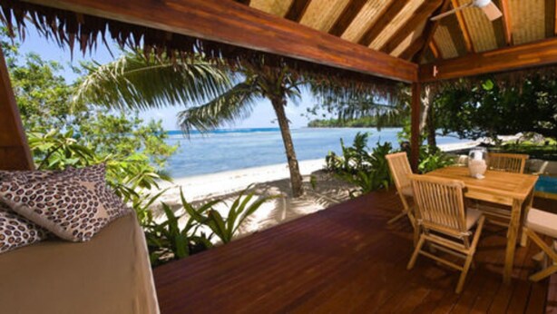Una terraza de madera con mesa y sillas con vista a una playa y al océano.